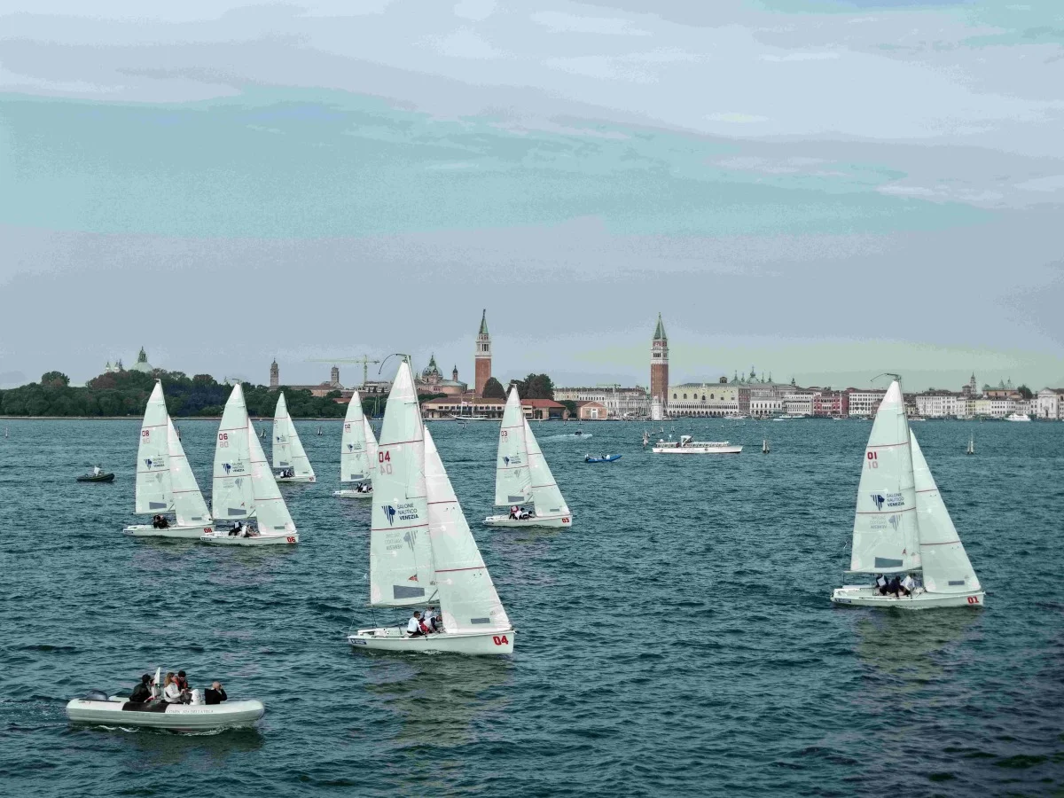 Flotta di derive con vele bianche in laguna, sullo sfondo il campanile di San Marco e San Giorgio; colori un po' slavati, formato 4:3.
