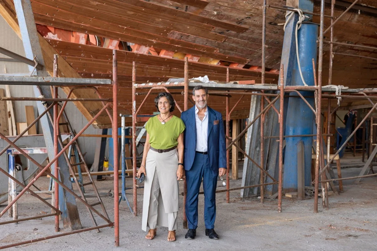 Due persone in abbigliamento formale davanti allo scafo in cantiere, posa per fotografia istituzionale