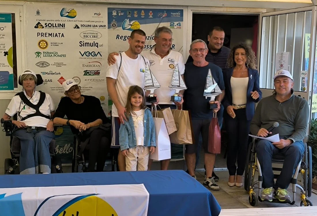 Premiazione su palco con vincitori che mostrano trofei e sfondo con sponsor; atmosfera ufficiale.