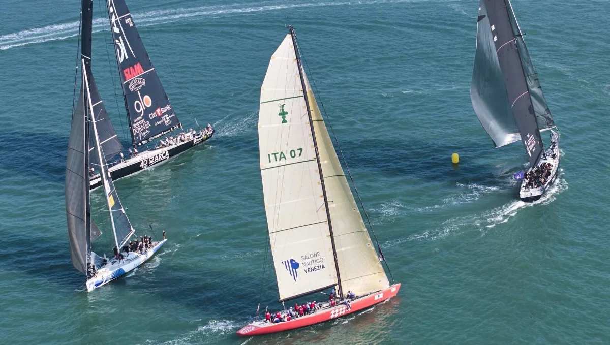 Inquadratura aerea di pi&ugrave; barche a vela in mare, scafo rosso con vela brandizzata, traiettorie e boa di gara.
