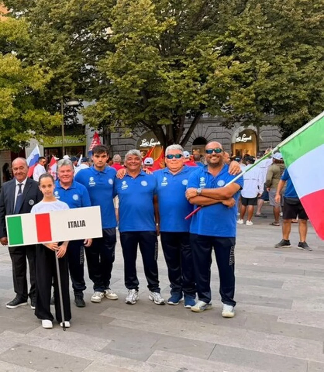 Foto di gruppo in piazza con la squadra italiana in divisa blu e cartello 'Italia', parziale panorama urbano