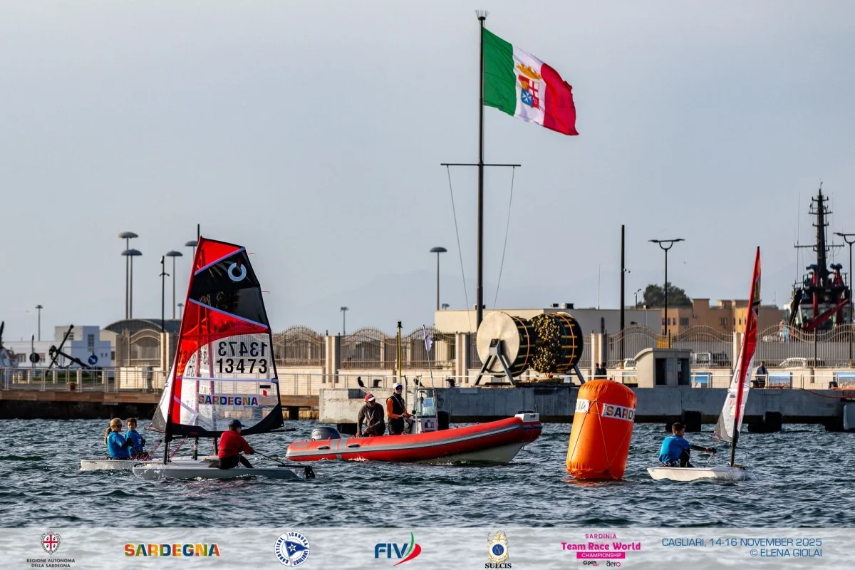 Windsurfer vicino a gommone rosso e boa arancione, con bandiera italiana della Marina che sventola sul molo di Cagliari.