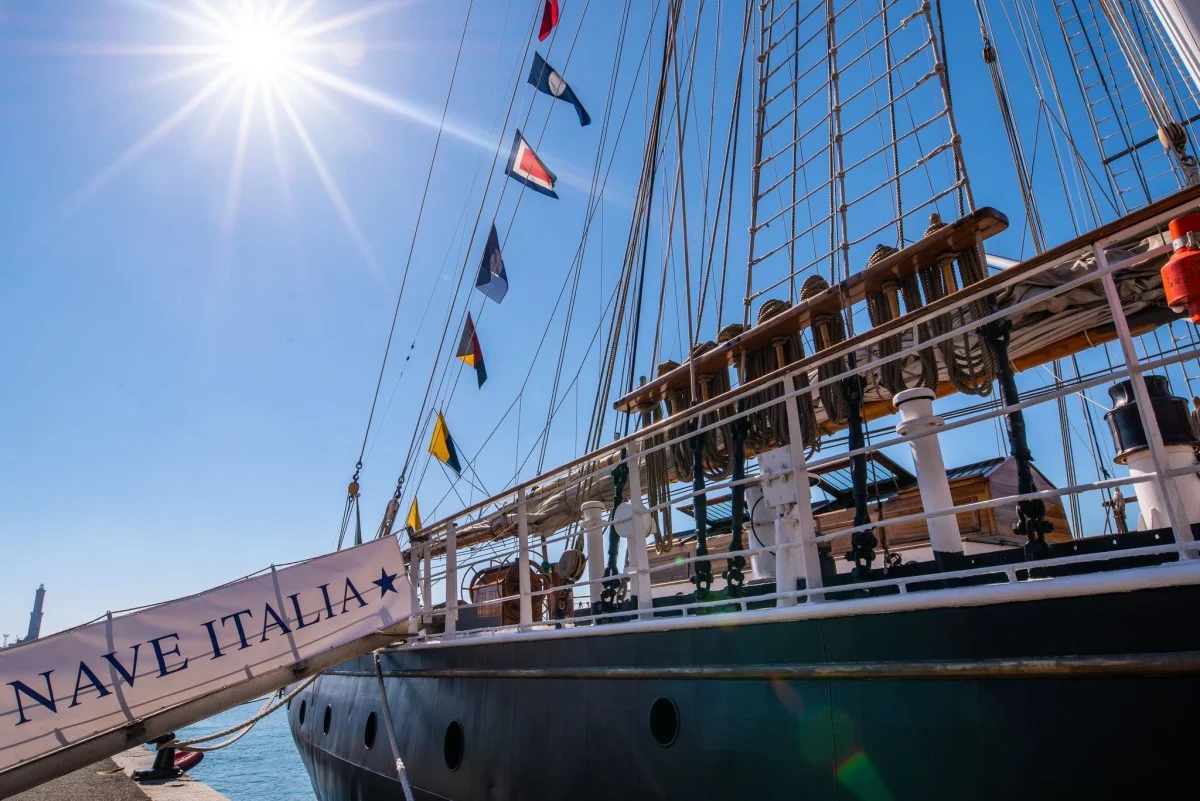 Dettaglio della fiancata e parapetto della goletta con scaletta d'imbarco recante la scritta ‘NAVE ITALIA’ e segnali nautici al sole.