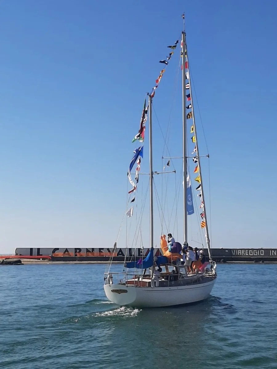Veliero d'epoca a due alberi pavesato con bandiere di segnalazione, con persone a bordo, in uscita dal porto di Viareggio sotto un cielo azzurro.