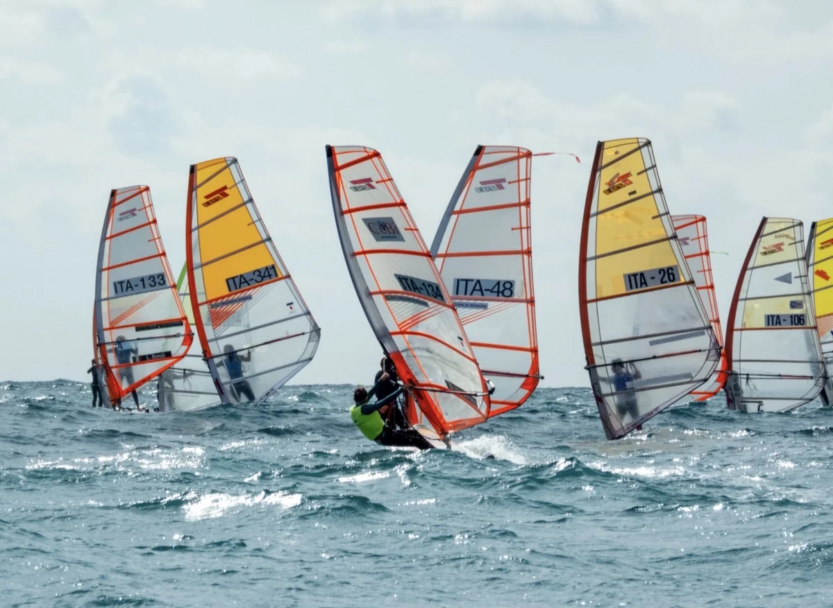 Regata di windsurf con vele gialle e trasparenti numerate ITA su mare increspato, vista da dietro.