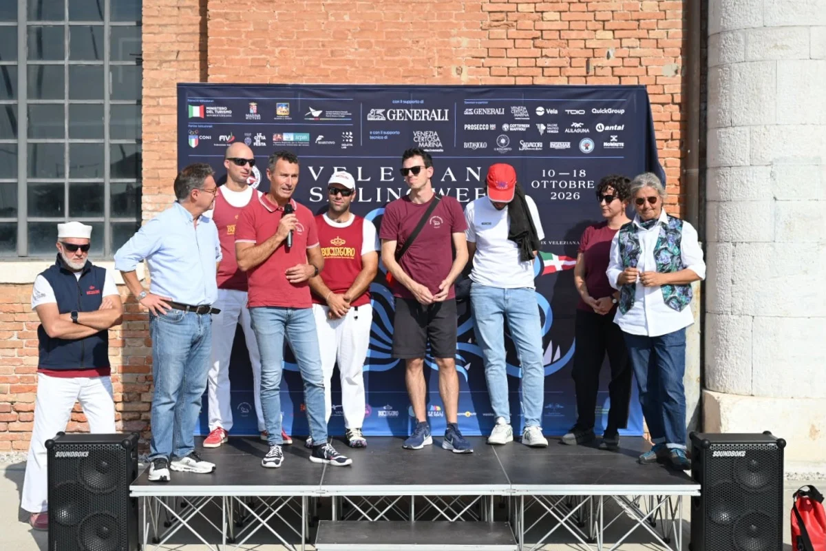 Cerimonia sul palco con persone, un microfono e backdrop Venice Sailing Week 10-18 ottobre 2026 con sponsor.