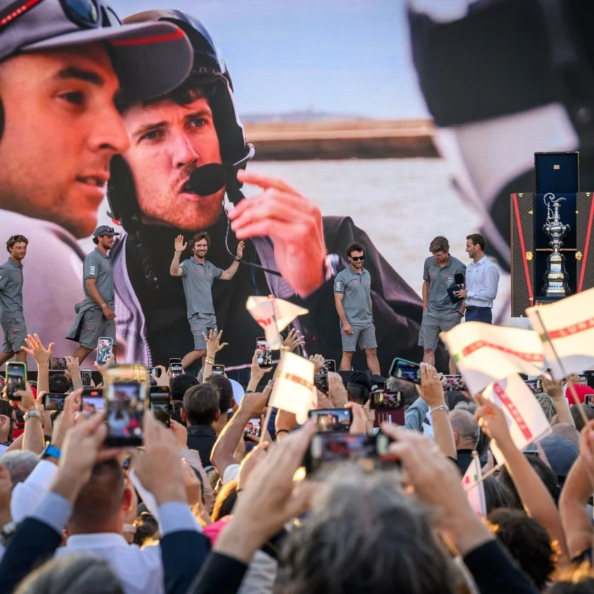 Palco con il team in cammino, folla che fotografa con smartphone e trofeo visibile: utile per cronaca e cerimonie.