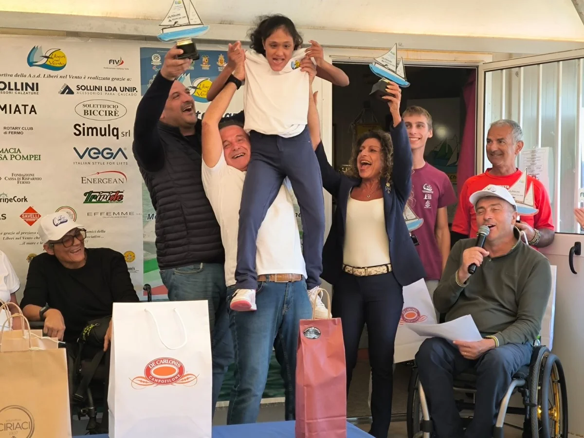 Momento di festa durante la premiazione: sollevamento di una bambina e applausi, emozione e inclusione.