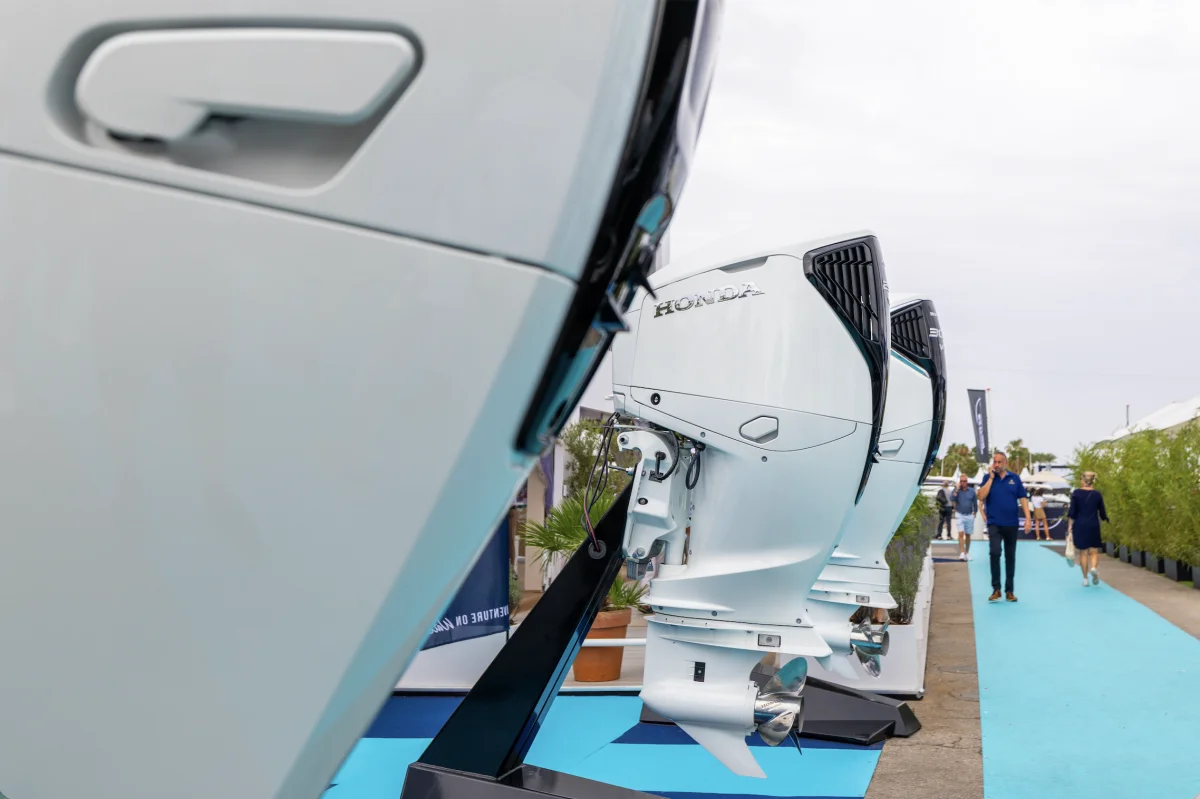 Primo piano di motori fuoribordo esposti su stand a un salone nautico, corridoio e visitatori sullo sfondo