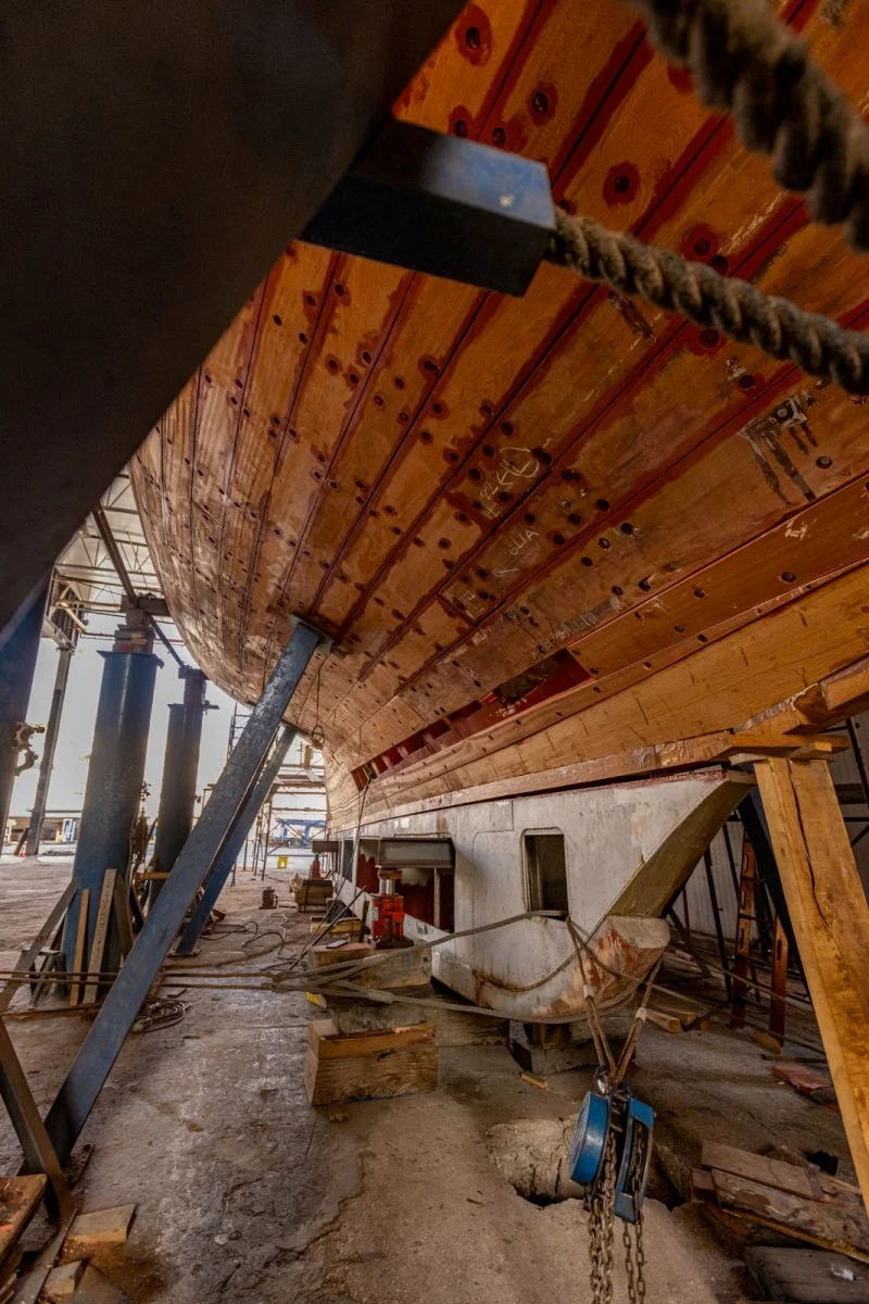 Veduta ravvicinata dello scafo in legno da sotto, officina con supporti e attrezzi, prospettiva dinamica
