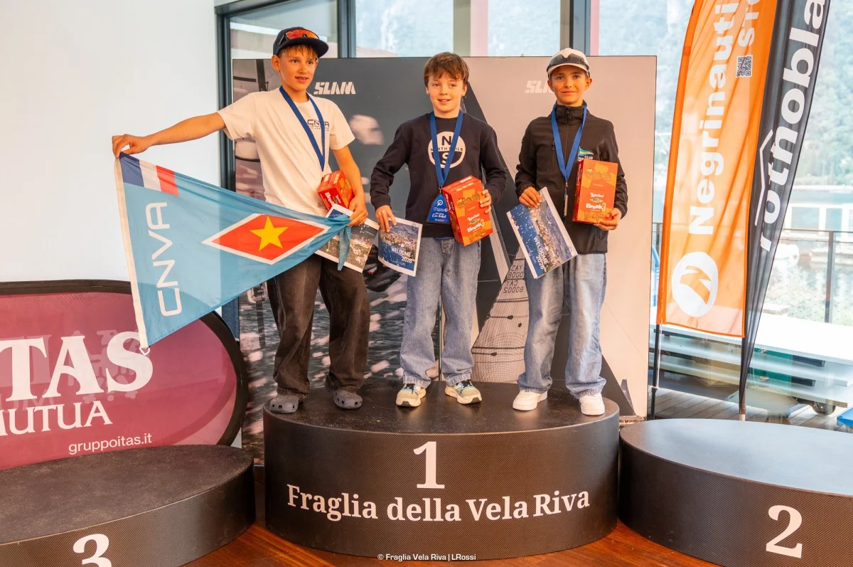Podio di tre giovani velisti con medaglie, premi e bandiera CNVA, sullo sfondo i banner degli sponsor.