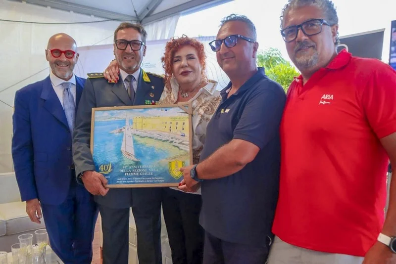 Cerimonia indoor: consegna di una targa tra ufficiali e organizzatori, atmosfera formale.