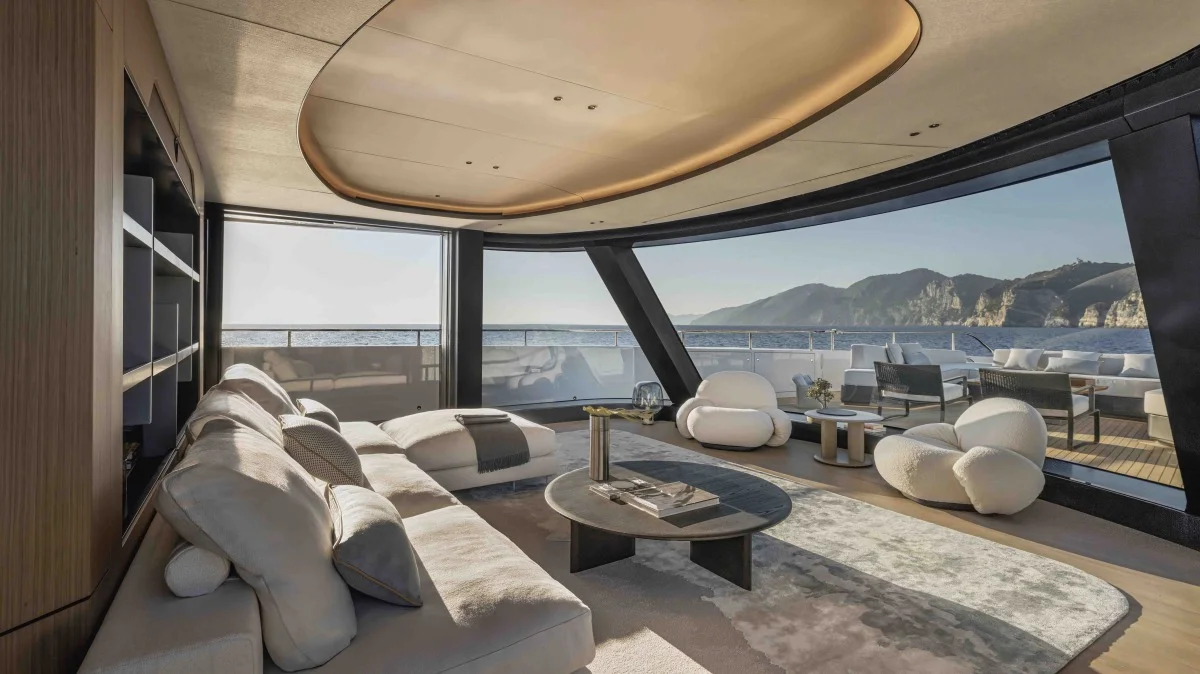 Salotto interno lussuoso con grandi vetrate panoramiche sul mare, arredi moderni e area esterna sul ponte posteriore.