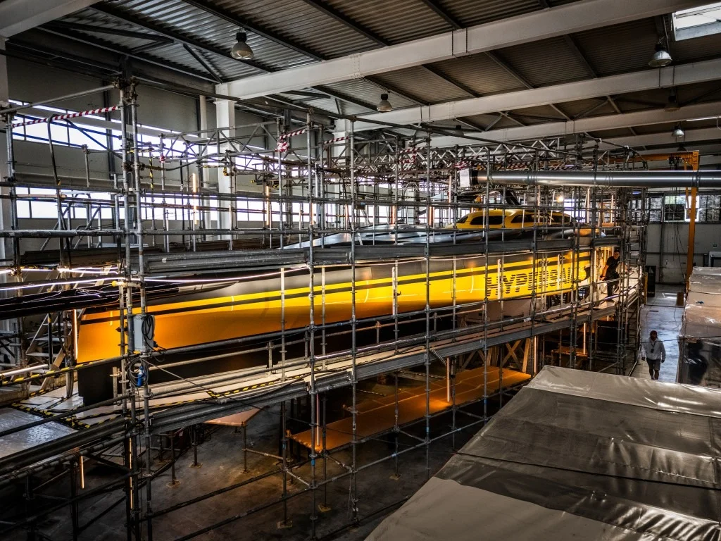 Interno del cantiere con lo scafo Hypersail avvolto da ponteggi e persone al lavoro, scritta gialla sulla fiancata.