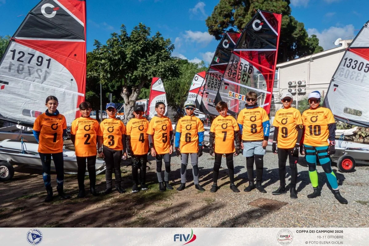 Ragazzi in maglie arancioni schierati davanti alle derive, ritratto di squadra in banchina