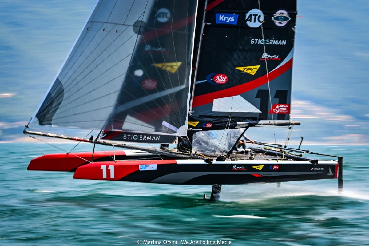 Primo piano dinamico di un catamarano foiling rosso e nero in planata ad alta velocità.