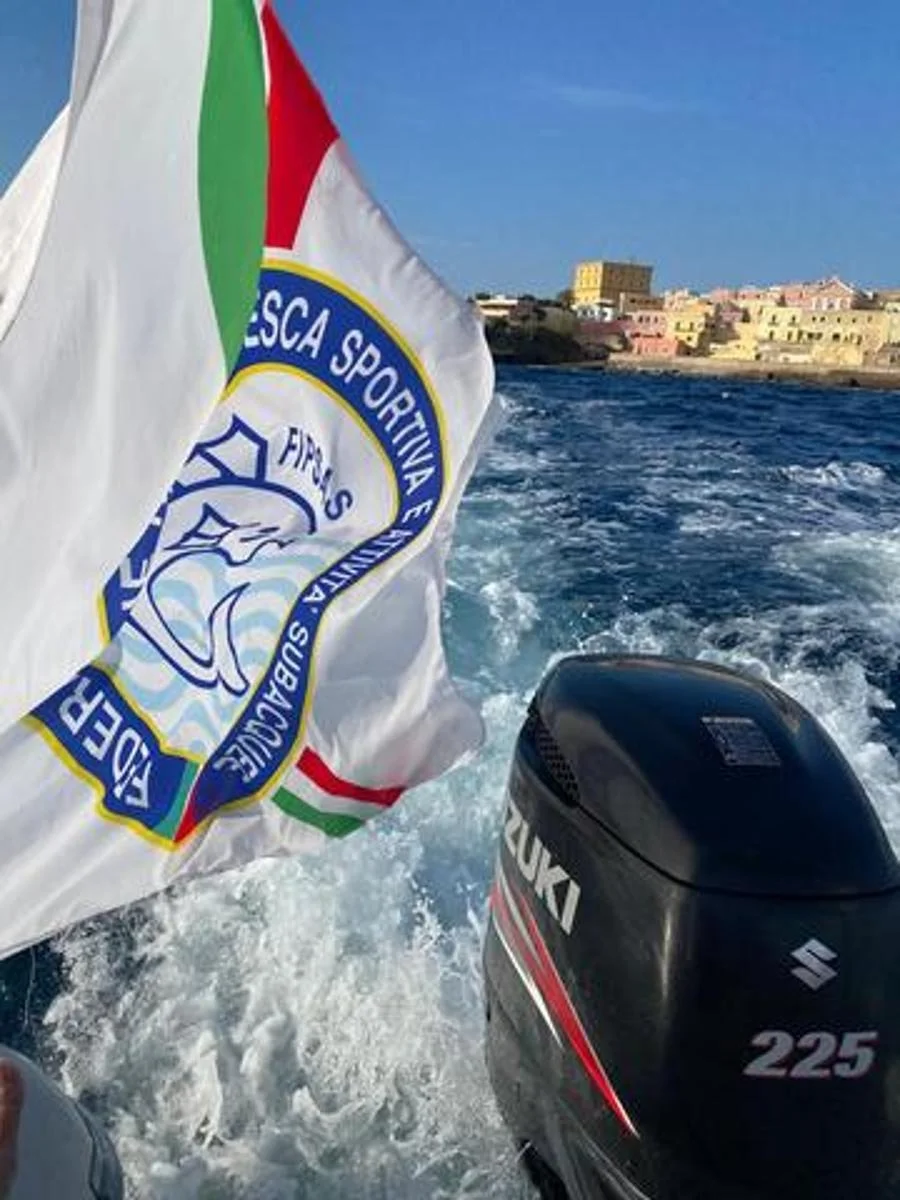 Bandiera FIPSAS al vento su un gommone con motore Suzuki 225, borgo colorato sullo sfondo. Foto verticale.