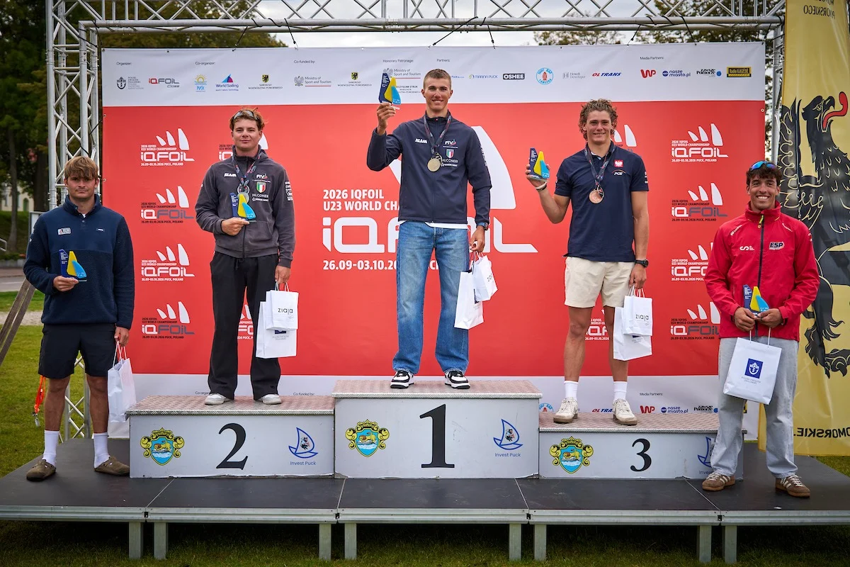 Podio con i vincitori dell'iQFoil U23, sfondo con logo evento e atleti che tengono trofei e borse.
