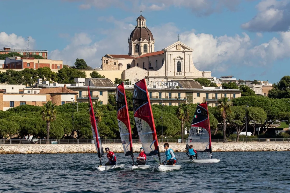 Quattro O'pen Skiff in navigazione davanti alla cupola di una chiesa e al verde del lungomare, cielo con nuvole.