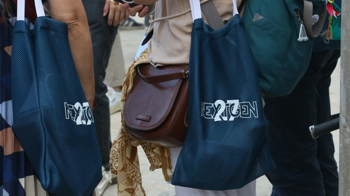 Primo piano di borse blu con logo 'NEXTGEN', dettaglio di merchandising o partecipanti all'evento.