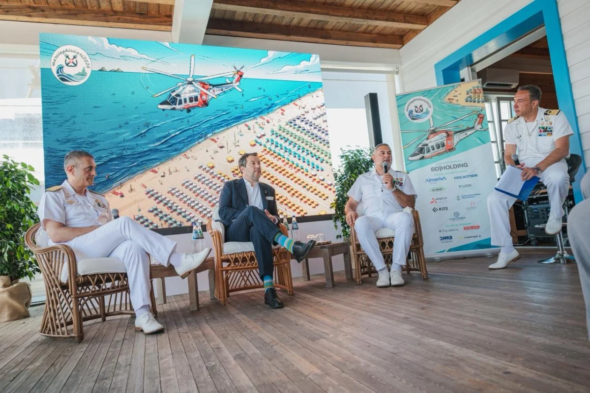 Tavola rotonda con ufficiali e relatore su palco, grande schermo alle spalle con immagine marina.