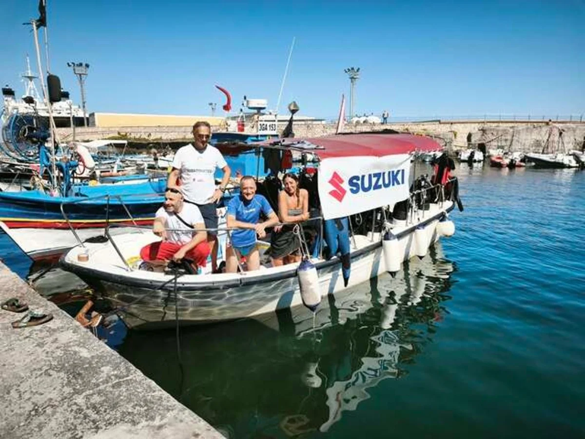 Gruppo di persone su una barca da immersione con banner Suzuki ormeggiata in porto.
