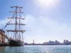 Brigantino a tre alberi attraccato al Porto Antico di Genova con skyline cittadino e sole