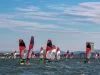 Numerose imbarcazioni con vele rosse e bianche in regata davanti alla costa di Rimini