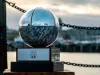 Trofeo a forma di sfera in pietra blu e metallo lucido su base in legno, con catene e specchio d'acqua sfocati sullo sfondo