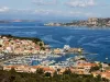 Panoramica di un porto turistico con marina, traghetti e case lungo una costa rocciosa.