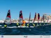 Fila di Open Skiff in regata davanti al lungomare di Cagliari con vele rosse e equipaggi in giubbotti fluorescenti