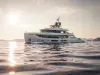 Yacht di lusso bianco in navigazione su mare calmo al tramonto, con il sole basso e colline sullo sfondo