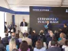 Cerimonia inaugurale con un relatore al podio davanti al pubblico seduto, sotto un tendone con schermo che riporta la data 22 ottobre