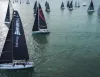 Veduta aerea di una flotta di barche a vela con vele scure in mare calmo; in primo piano uno yacht con la scritta Gruppo Hera EstEnergy.