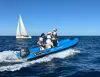 Gommone azzurro con tre persone a bordo e motore Yamaha in navigazione, barca a vela sullo sfondo