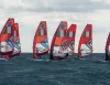 Windsurf con vele arancioni e bandiera italiana in fila su mare mosso sotto un cielo nuvoloso