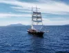 Veliero a tre alberi con le vele spiegate che solca il mare blu verso isole all'orizzonte