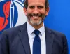 Uomo sorridente con barba, giacca e cravatta blu con ancora dorata, davanti a un fondale blu con logo parziale di Assonautica