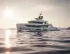Yacht di lusso bianco in navigazione su mare calmo al tramonto, con il sole basso e colline sullo sfondo
