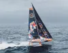 IMOCA foiling con vele scure e scafo colorato che sfreccia sollevato sui foil su un mare grigio, con la scritta 11th Hour Racing