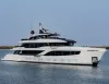 Superyacht bianco su più ponti in navigazione su acqua calma, con costa bassa sullo sfondo e cielo sereno