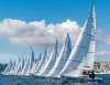 Fila di barche a vela J/22 in regata davanti al lungomare di Napoli con cielo sereno.