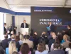 Cerimonia inaugurale con un relatore al podio davanti al pubblico seduto, sotto un tendone con schermo che riporta la data 22 ottobre