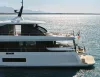 Yacht Azimut bianco in navigazione, vista laterale della poppa con terrazze, flybridge e bandiera italiana, su mare calmo con costa sullo sfondo