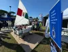 Simulatore di Optimist con vela tricolore su pedana, bambini a bordo e visitatori intorno, accanto a un banner blu della Lega Navale