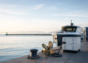 Banchina al tramonto con elica in bronzo, unità di accumulo collegata con cavo, colonnina di ricarica e barca ormeggiata sul mare