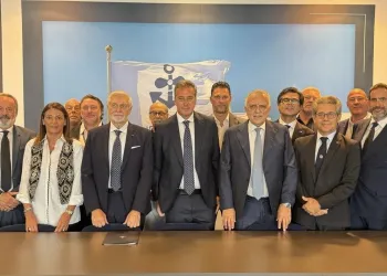 Gruppo di membri del Consiglio direttivo in piedi dietro un tavolo con bandiera marina sullo sfondo