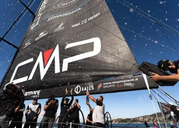 Equipaggio a poppa su una barca con grande vela nera mentre festeggia a bordo