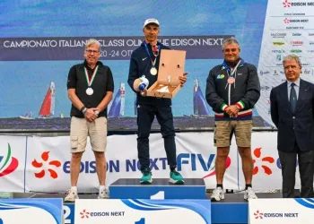 Tre velisti con medaglie sul podio, quello centrale regge una scatola di legno; a destra un uomo in giacca e cravatta, sullo sfondo i loghi Edison Next.