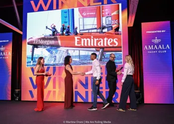 Premiazione su palco con schermo che mostra un catamarano Emirates e persone che si stringono la mano